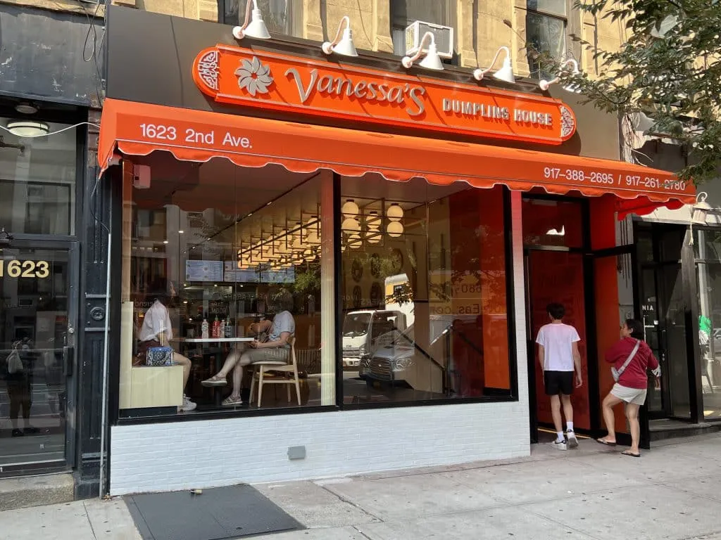 Vanessa’s Dumpling House on Second Avenue, with an orange sign and awning over a glass storefront.