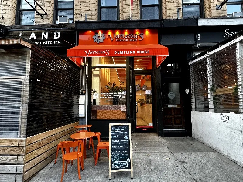 Vanessa’s Dumpling House on Amsterdam Avenue, with an orange awning, orange chairs outside and a chalkboard sign.