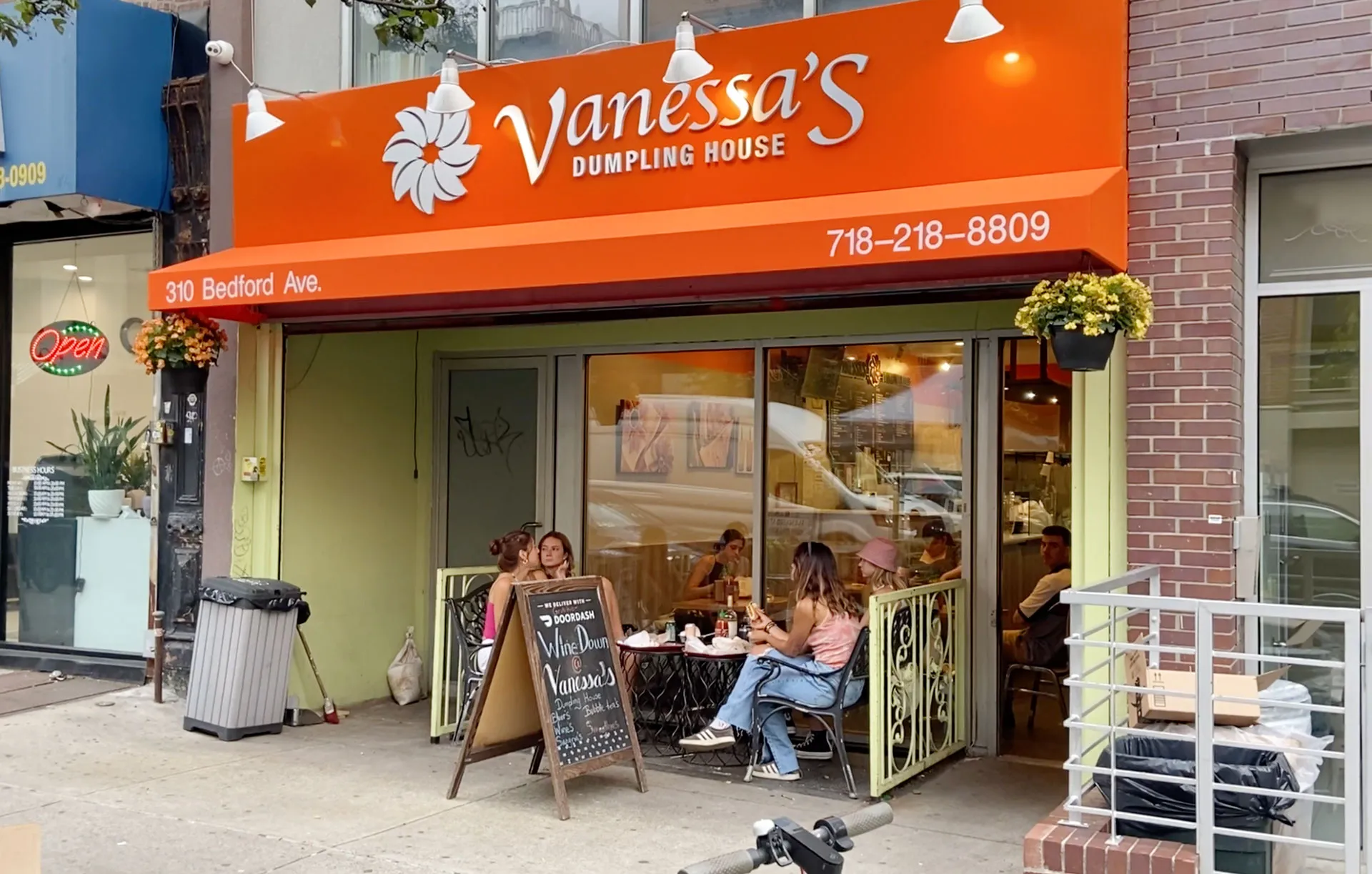 Vanessa’s Dumpling House on Bedford Avenue, with an orange sign and awning and guests seated at the window.
